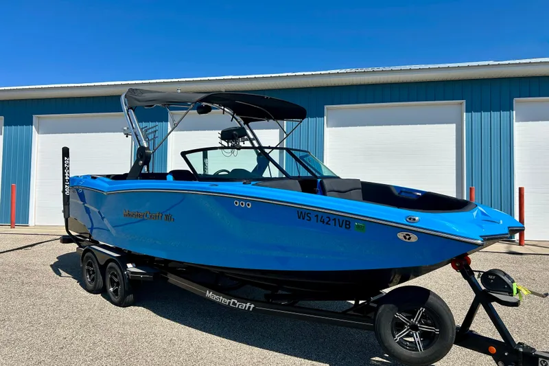 The Image of 2021 MasterCraft NXT24 boat in vibrant blue on trailer, parked near blue building. - 1