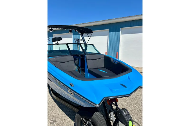 Slide: The Image of 2021 MasterCraft NXT24 boat in vibrant blue, parked outdoors near a blue building. - 10