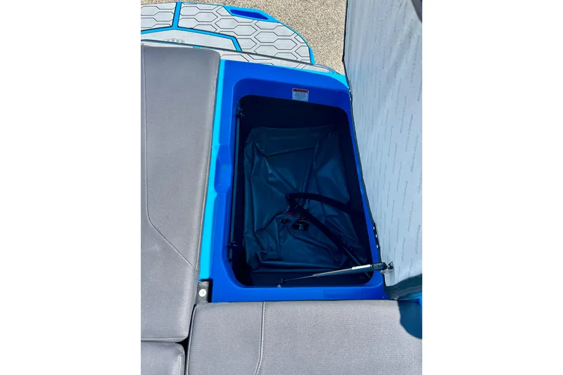 Slide: The Image of Open storage compartment in 2021 MasterCraft NXT24 boat, featuring blue interior and hydraulic lift. - 22