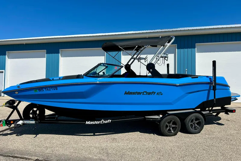 Slide: The Image of 2021 MasterCraft NXT24 boat in vibrant blue, parked on a trailer outside a blue building. - 4