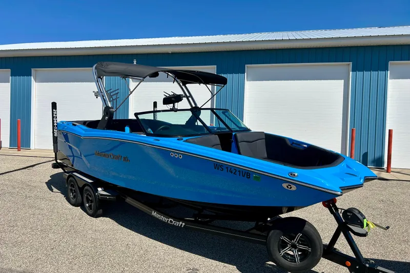 Slide: The Image of 2021 MasterCraft NXT24 boat in vibrant blue, parked on a trailer near blue storage units. - 5