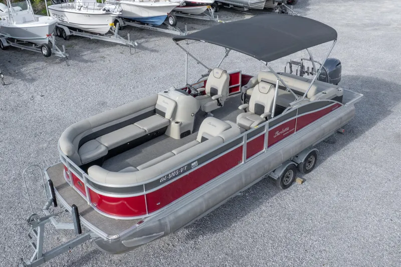 Slide: The Image of 2021 Barletta C24UC pontoon boat with red exterior and spacious seating, parked on gravel. - 13