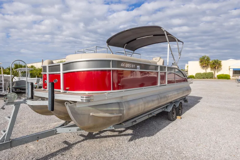 Slide: The Image of 2021 Barletta C24UC pontoon boat with red exterior on a trailer, parked outdoors. - 17