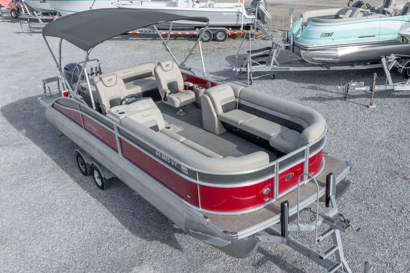 Slide: The Image of 2021 Barletta C24UC pontoon boat with red exterior and spacious seating, parked on a trailer. - 2