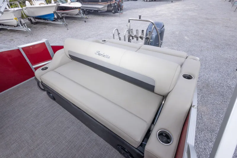 Slide: The Image of 2021 Barletta C24UC pontoon boat with beige seating and cup holders, parked on gravel. - 23