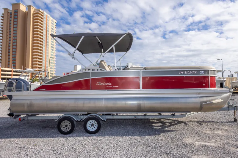 Slide: The Image of 2021 Barletta C24UC pontoon boat with red exterior, parked on a trailer. - 3