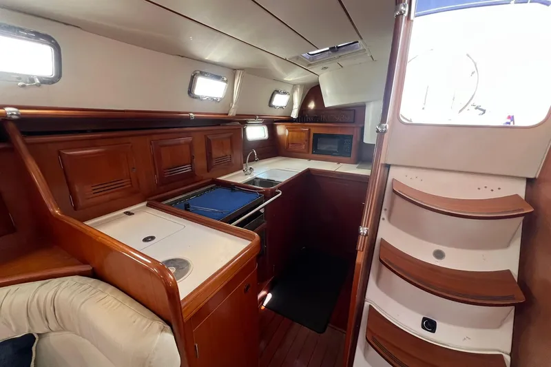 Slide: The Image of Interior of 2001 Beneteau Oceanis 461 yacht, featuring a compact kitchen with wooden cabinetry. - 25