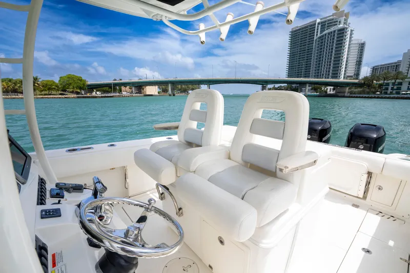 Slide: The Image of 2013 Boston Whaler 320 Outrage boat interior with dual seats, steering wheel, and scenic waterfront view. - 16