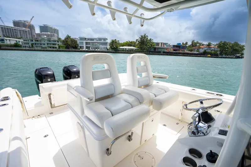 Slide: The Image of 2013 Boston Whaler 320 Outrage boat interior with dual seats and steering wheel, docked by waterfront homes. - 17