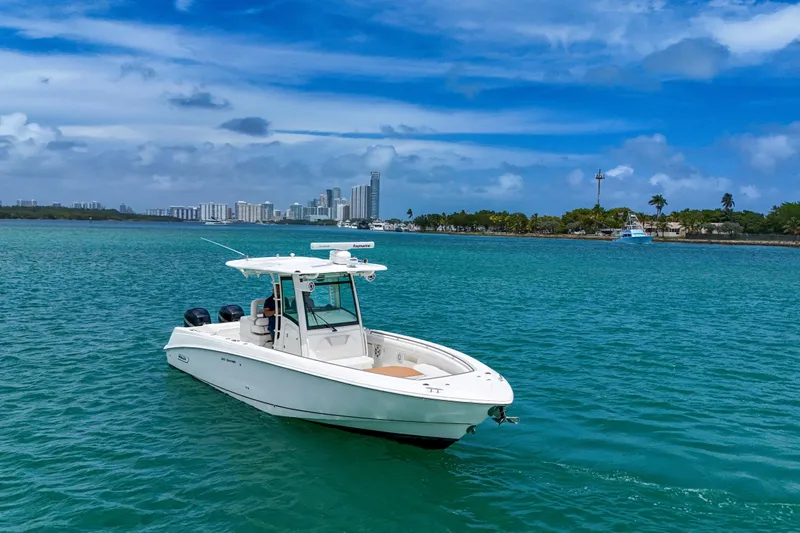 Slide: The Image of 2013 Boston Whaler 320 Outrage boat on turquoise water with city skyline backdrop. - 3