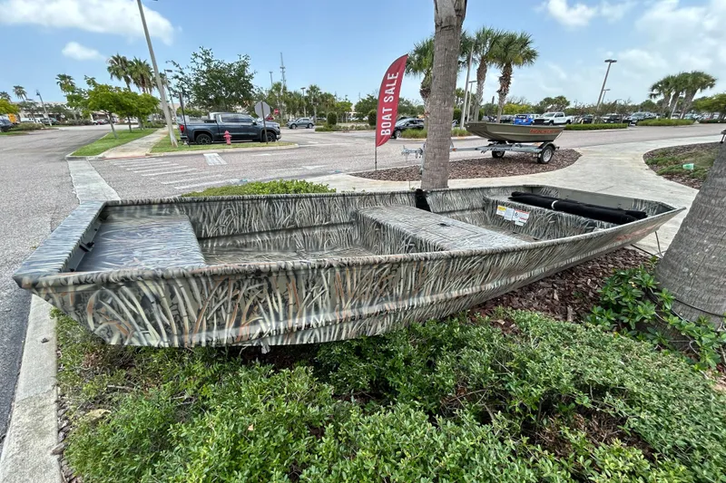 The Image of 2026 Tracker Grizzly 15 Jon boat on display, camo design, outdoor setting, boat sale sign. - 0