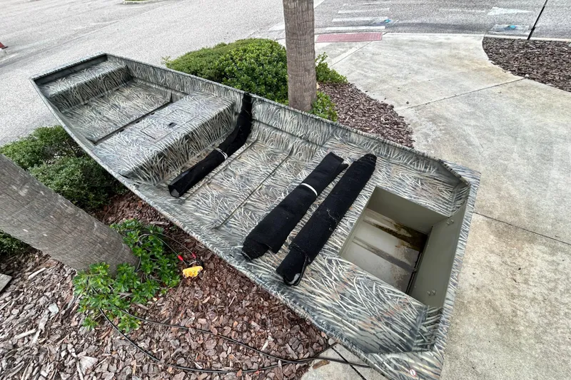 Slide: The Image of 2026 Tracker Grizzly 15 Jon boat with camouflage design on a concrete surface. - 2