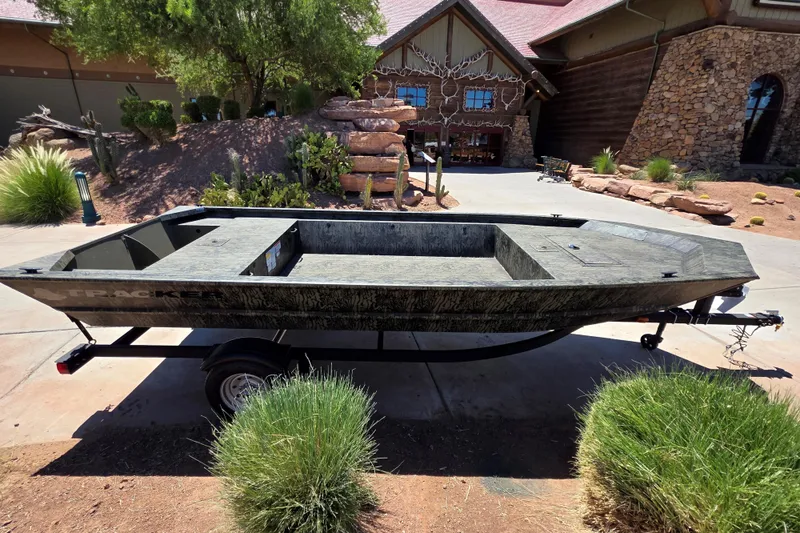The Image of 2026 Tracker Grizzly 1648 Utility boat on trailer, parked in a residential driveway. - 0
