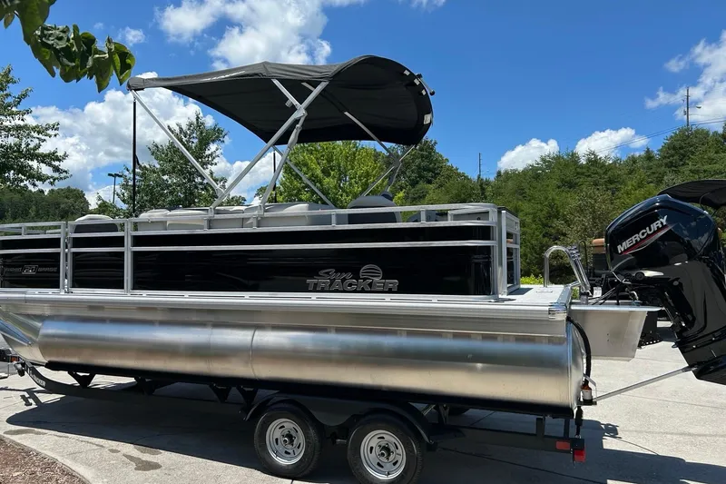 The Image of 2026 Sun Tracker Fishin' Barge 20 DLX pontoon boat on trailer, under clear blue sky. - 0