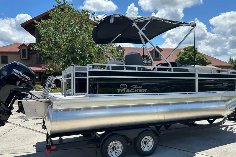 Slide: The Image of 2026 Sun Tracker Fishin' Barge 20 DLX pontoon boat on trailer, parked outdoors. - 2