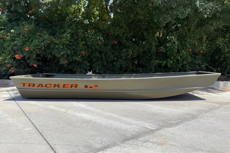 Slide: The Image of 2026 Tracker Grizzly 12 Jon boat on concrete, surrounded by lush greenery. - 3