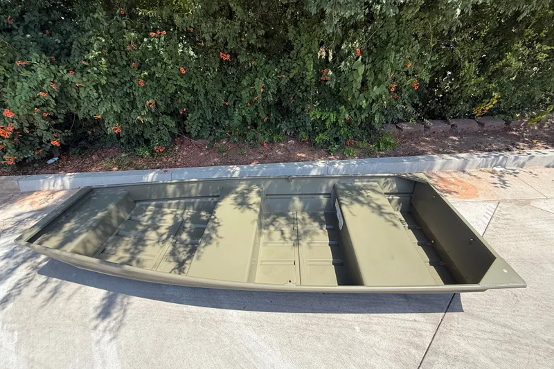 Slide: The Image of 2026 Tracker Grizzly 12 Jon boat on pavement, surrounded by greenery. - 2