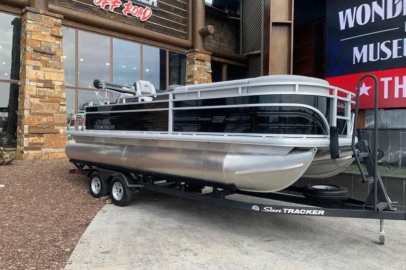 The Image of 2026 Sun Tracker SportFish 20 DLX pontoon boat on trailer outside showroom. - 0