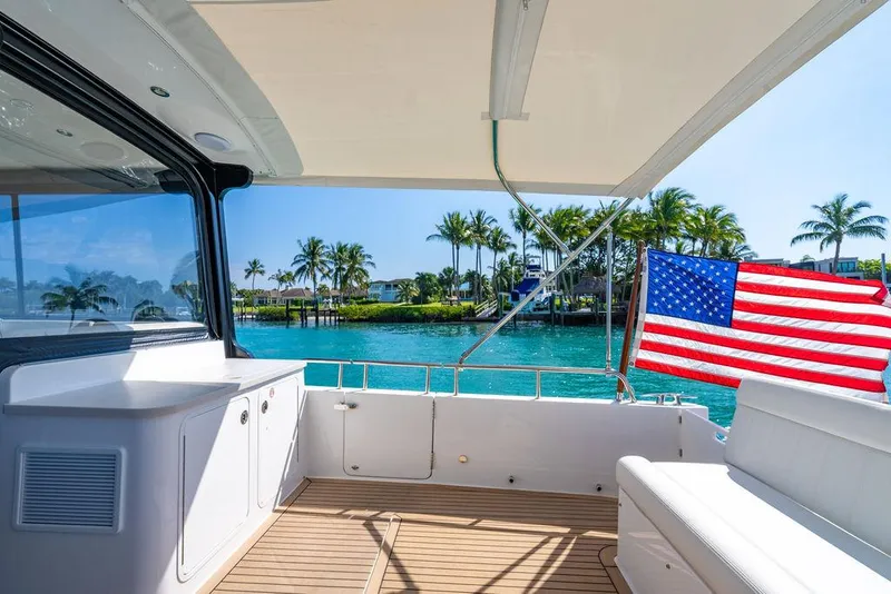 Slide: The Image of 2024 MJM 4 yacht deck with American flag, overlooking tropical waters and palm trees. - 24