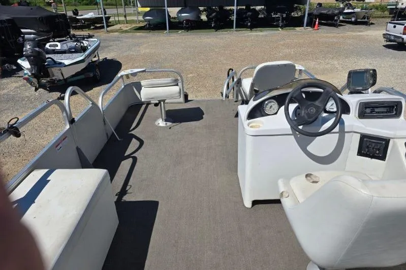 Slide: The Image of 2004 Bandit Pontoon boat interior with steering console and seating, parked on gravel. - 7