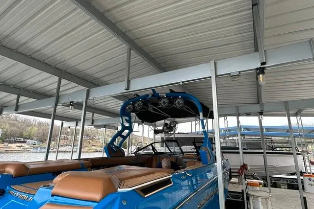 Slide: The Image of 2020 Nautique Super Air Nautique G25 boat in dock, featuring blue exterior and brown seating. - 2