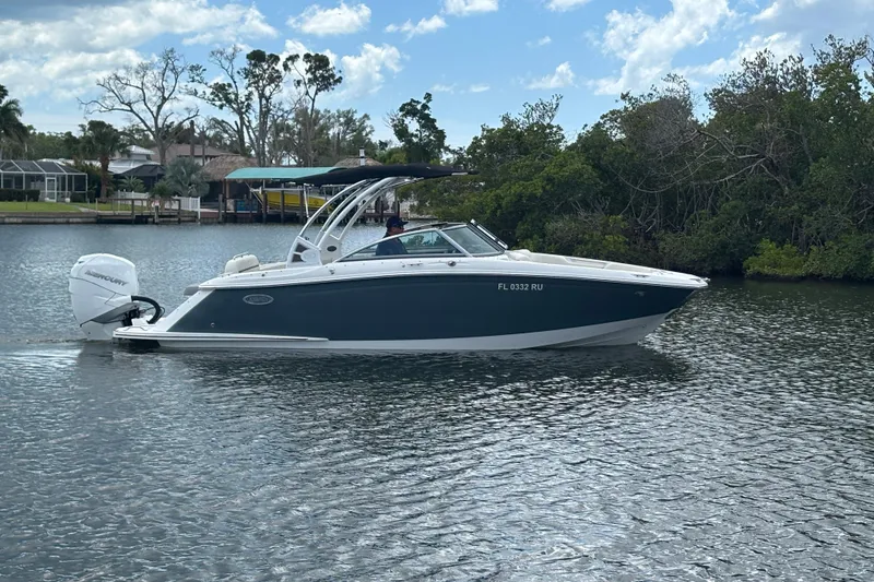 The Image of 2019 Cobalt 23SC boat cruising on a calm river with lush greenery. - 1