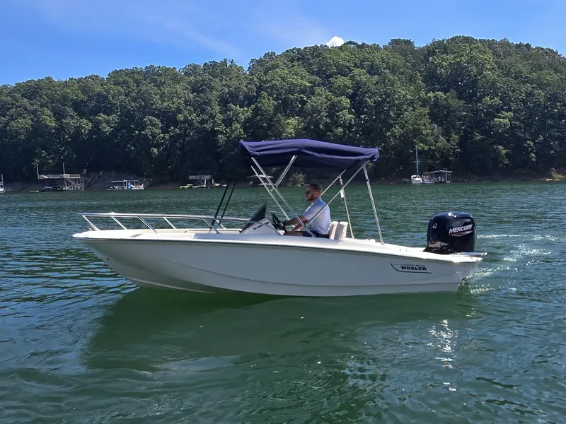 Slide: The Image of A 2026 Boston Whaler 160 Super Sport cruising on a calm lake with a wooded shoreline. - 0