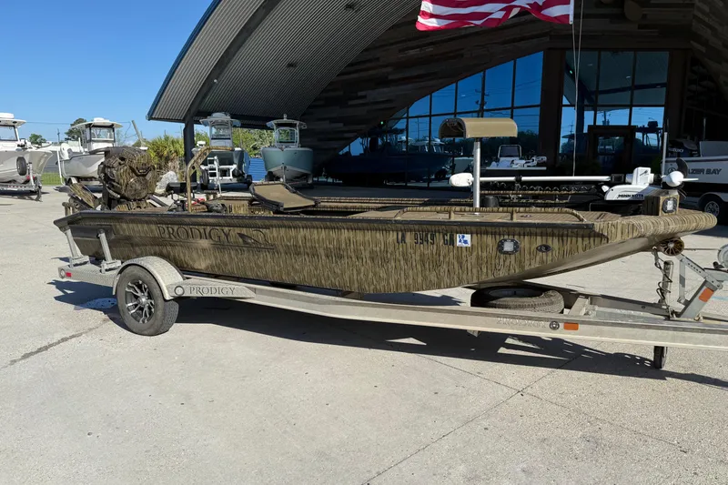 Slide: The Image of 2022 Prodigy 1854 boat on trailer outside a showroom with American flag. - 1