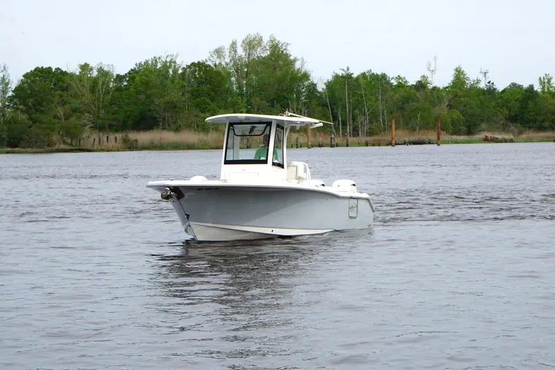 Slide: The Image of 2025 Sea Hunt Ultra 265 SE boat on calm water with lush green shoreline. - 5