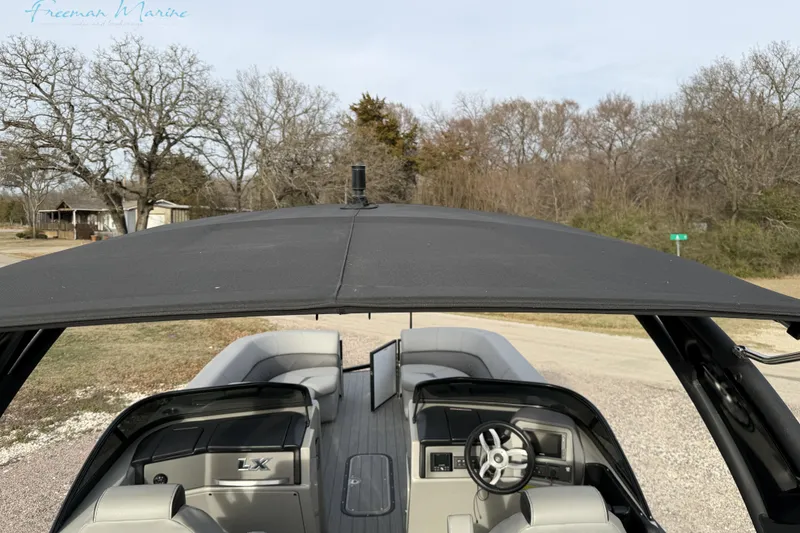 Slide: The Image of 2022 Manitou 27 LX SRW pontoon boat with canopy, parked on a rural road. - 26