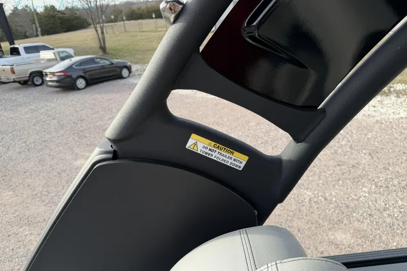 Slide: The Image of 2022 Manitou 27 LX SRW boat interior with caution label, parked cars in background. - 27