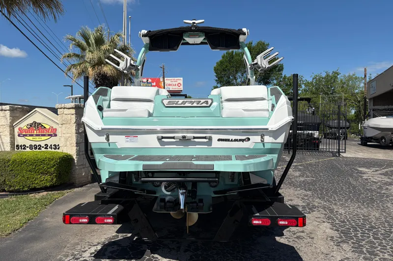Slide: The Image of 2026 Supra SA 550 boat in dealership lot, rear view with teal and white design. - 7