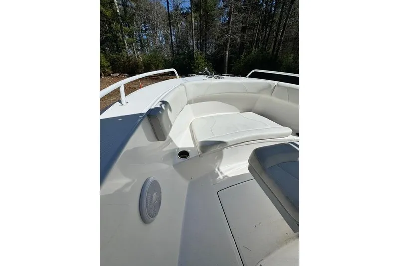 Slide: The Image of 2021 Edgewater 208CC boat interior with white seating and speaker, surrounded by trees. - 17
