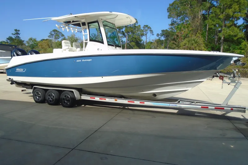 Slide: The Image of 2011 Boston Whaler 330 Outrage boat on trailer, blue hull, parked outdoors. - 5