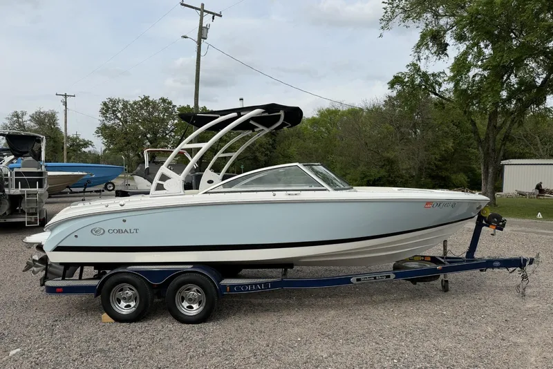 The Image of 2016 Cobalt 220 boat on trailer, parked outdoors, with trees and other boats in the background. - 0