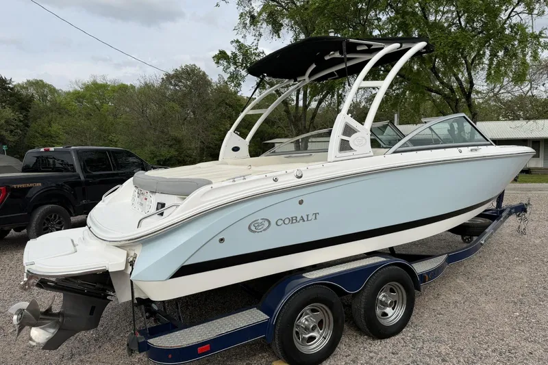 Slide: The Image of 2016 Cobalt 220 boat on trailer, parked outdoors with trees in the background. - 2