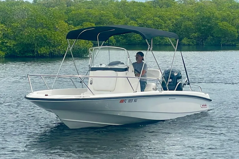 Slide: The Image of 2008 Boston Whaler 200 Dauntless boat cruising on a calm lake with lush greenery. - 2