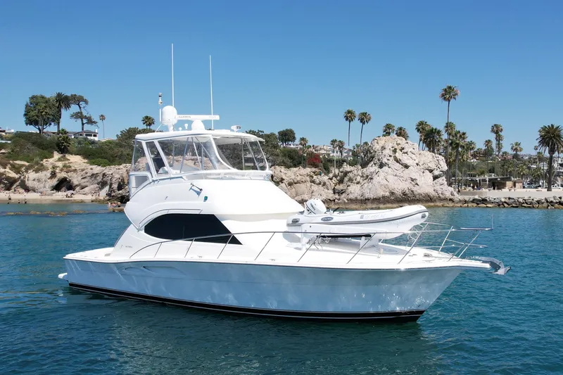 Slide: The Image of 2003 Riviera 40 Flybridge yacht cruising near rocky coastline with palm trees. - 6