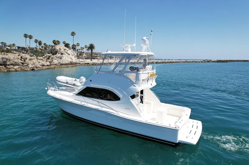 Slide: The Image of 2003 Riviera 40 Flybridge yacht cruising in clear blue waters near rocky shoreline. - 8