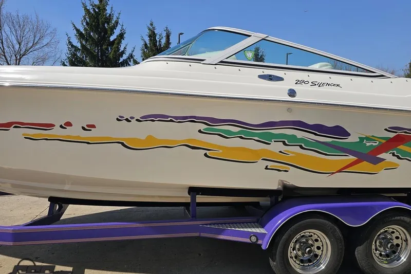 Slide: The Image of 2001 Powerquest 280 Silencer boat with colorful graphics on a purple trailer. - 19