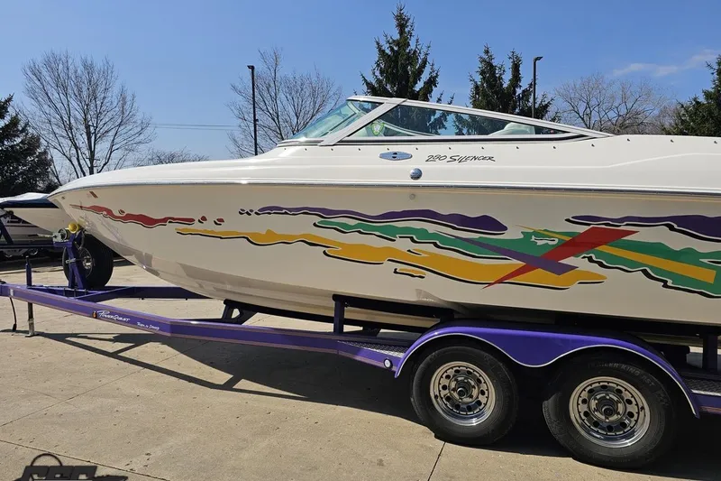 Slide: The Image of 2001 Powerquest 280 Silencer boat on trailer with colorful graphics, parked outdoors. - 22