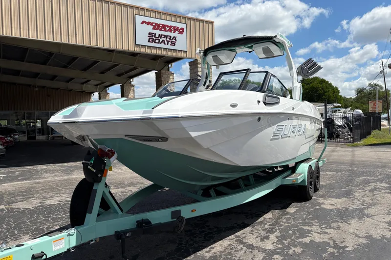 Slide: The Image of 2026 Supra SE 550 boat on trailer at dealership, under clear blue sky. - 4