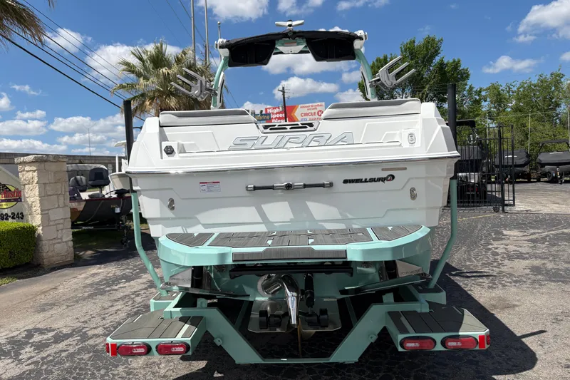 Slide: The Image of 2026 Supra SE 550 boat rear view, featuring Swell Surf system, parked outdoors. - 9