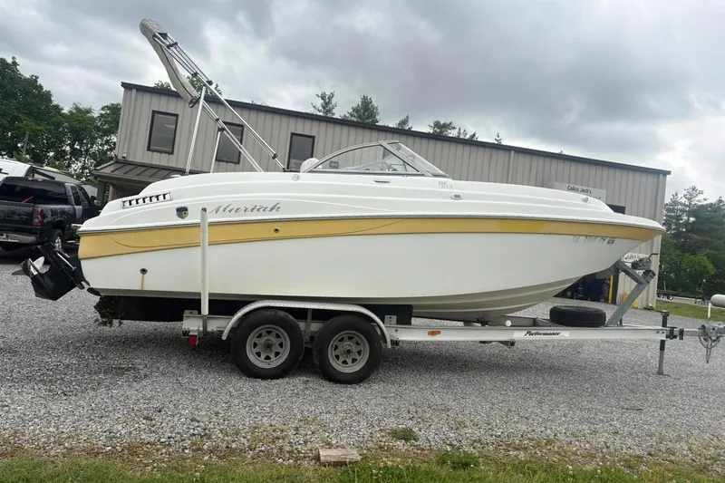 The Image of White and yellow 2004 Mariah DX213 boat on trailer, parked on gravel near a building. - 0