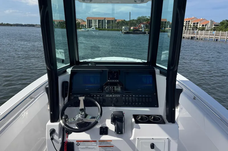 Slide: The Image of 2025 Blackfin 252 CC boat dashboard with steering wheel and navigation screens on the water. - 15