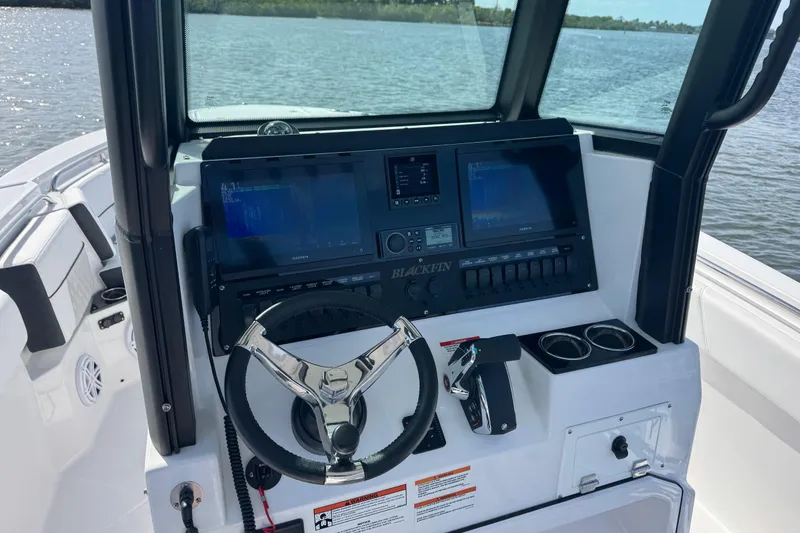 Slide: The Image of 2025 Blackfin 252 CC boat dashboard with steering wheel and dual displays on a sunny day. - 24