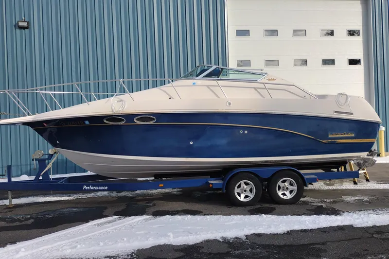 The Image of 1996 Crownline 250 CR boat on trailer, parked outside a blue industrial building. - 1