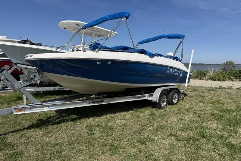 The Image of 2021 Stingray 212 SC boat on trailer, blue and white, parked on grass. - 8