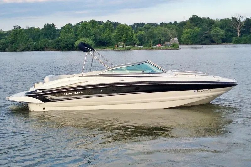 The Image of 2007 Crownline 252 EX boat on a calm lake with lush green shoreline. - 1