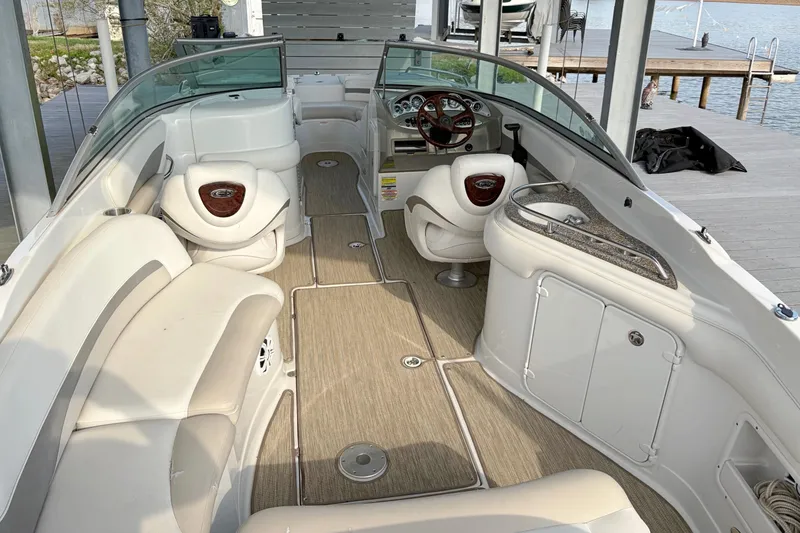 Slide: The Image of 2007 Crownline 252 EX boat interior with beige seating and wooden accents, docked by the water. - 8